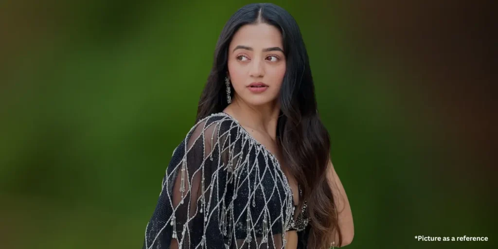 A stylish actress Helly Shah dressed in a glamorous black outfit embellished with shimmering silver tassels, gazing sideways with an elegant expression.