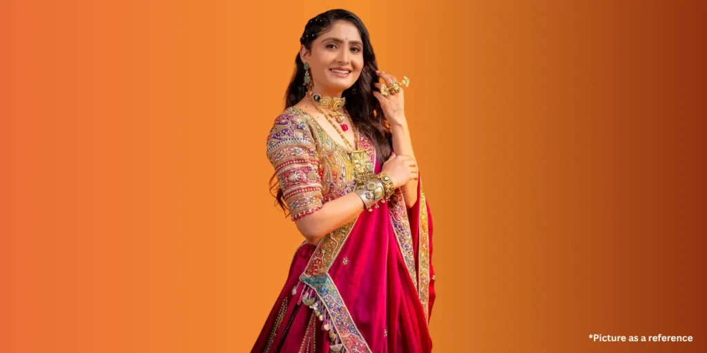 A woman, Geetaben Rabari, adorned in a regal magenta and gold embroidered lehenga choli with traditional jewelry, smiling confidently against an orange gradient backdrop.