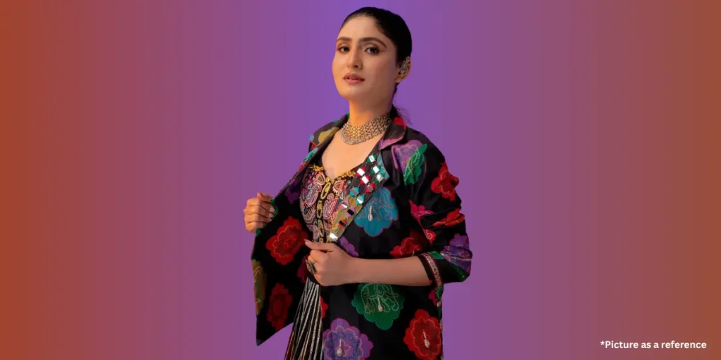Gujarati folk singer Geeta Rabari, wearing a colorful embroidered jacket and jewelry, poses against a purple gradient background.