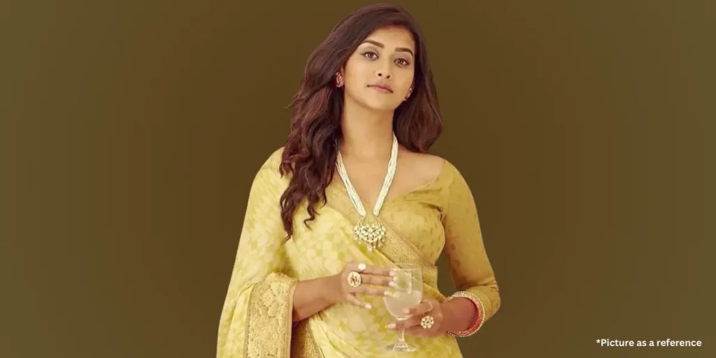 Pooja Jhaveri in a yellow saree, holding a glass, wearing elegant jewelry.