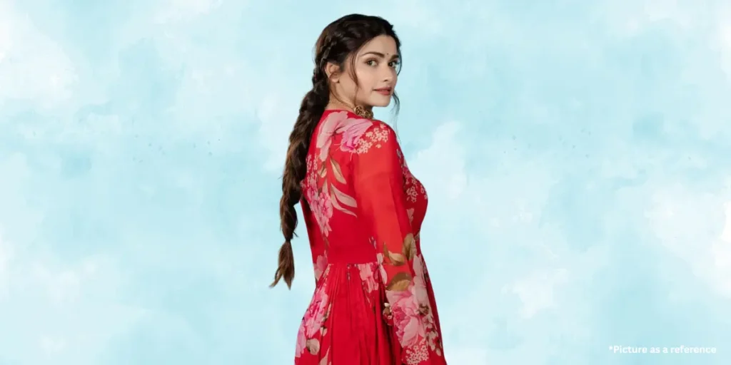 Prachi Desai is in a traditional red floral dress with a long braid, looking back gracefully against a pastel blue background.