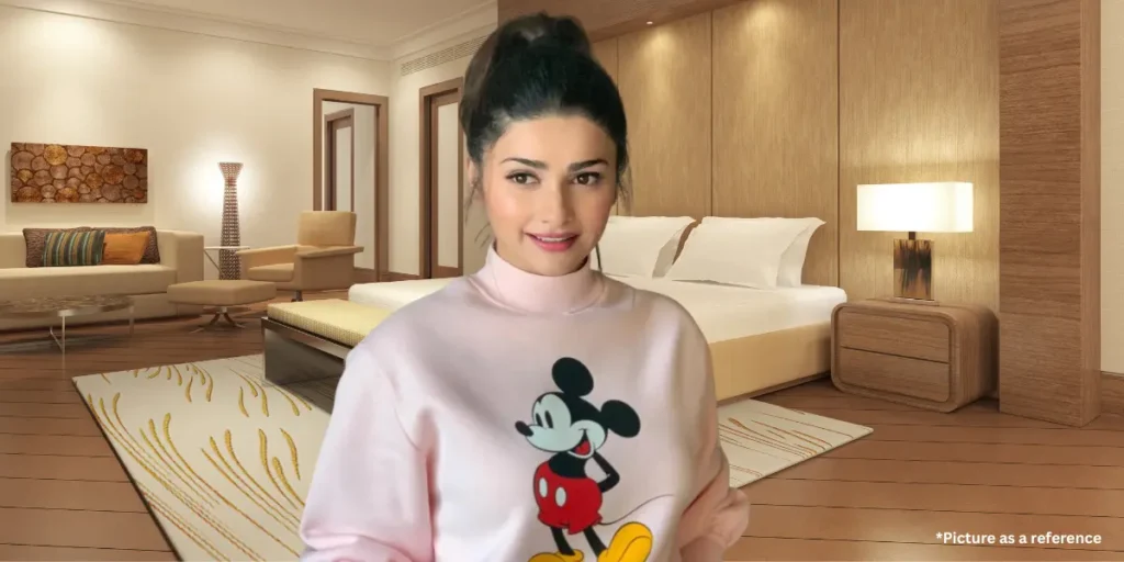 Prachi Desai is smiling and wearing a cute Mickey Mouse sweatshirt, posing in a modern luxury bedroom.