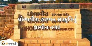 A signboard with the text Dholavira Harappan City in Gujarati, Hindi, and English. A Gujarati text, "ધોળાવીરા હરપ્પન સંસ્કૃતિનું પ્રાચીન નગર," is at the center of the image. On the left bottom side, there is a brand logo of MitroMate.