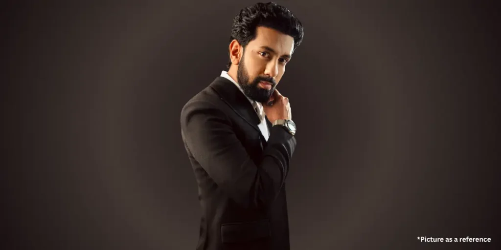 Actor Mitra Gadhvi in a black suit, adjusting his collar while wearing a wristwatch on a dark background