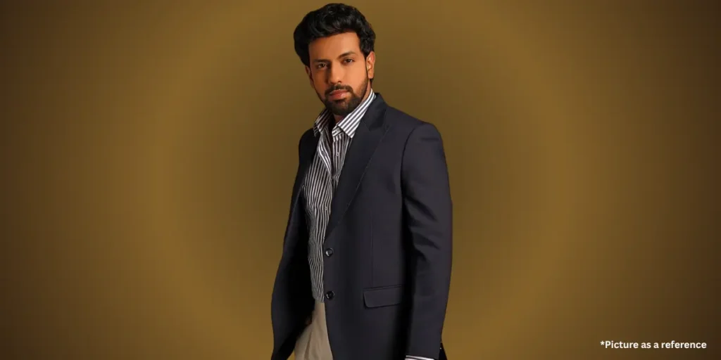 Gujarati actor and writer Mitra Gadhvi, wearing a black blazer with a striped shirt posing confidently on a brown background