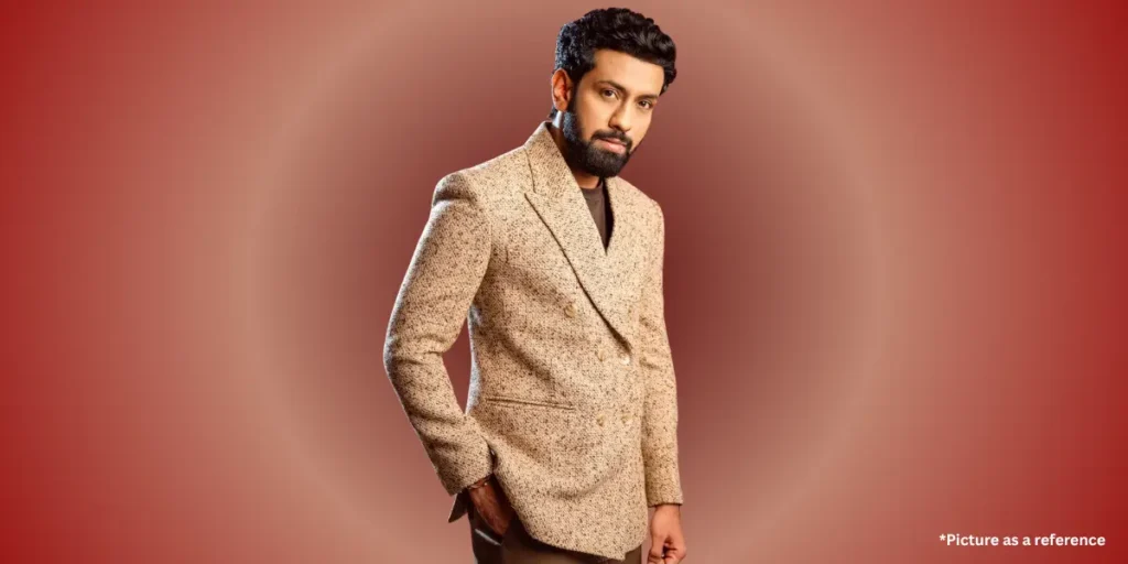 Indian actor Mitra Gadhvi in a beige double-breasted blazer, posing with hands in pockets on a red gradient background