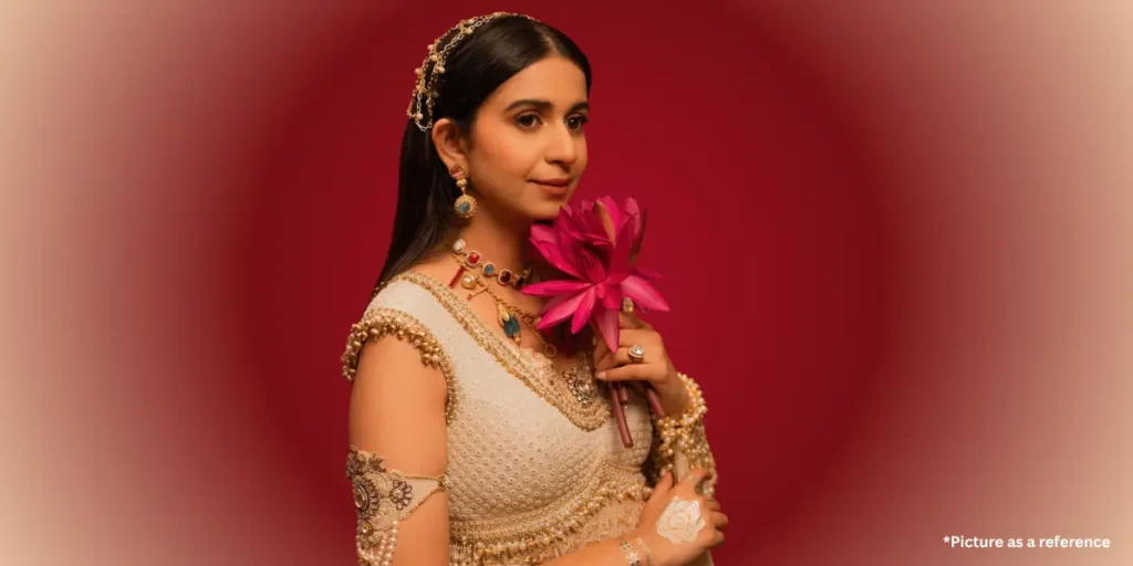 Indian singer Kinjal Dave in an elegant white and gold traditional outfit, holding a pink lotus flower.