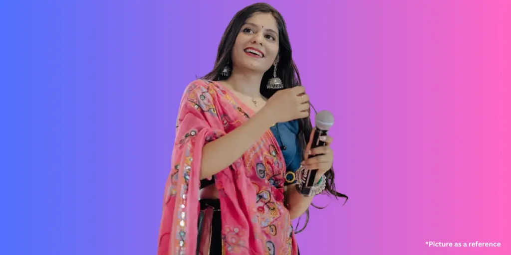 Aarti Sangani is performing with a microphone, wearing a vibrant pink embroidered dupatta and heavy jhumka earrings.