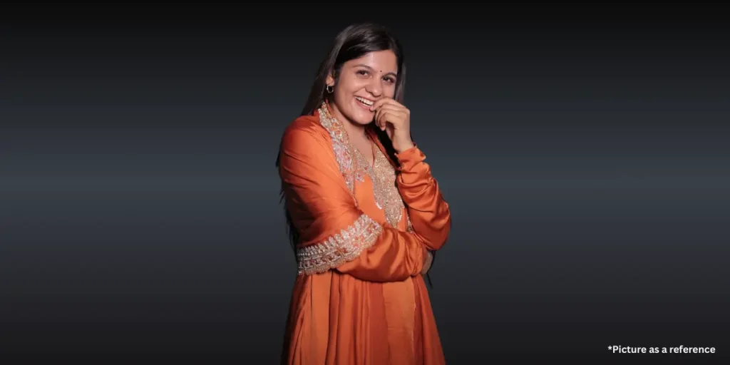 Aarti Sangani laughing and posing in a burnt orange traditional Indian dress against a dark grey vignette background.