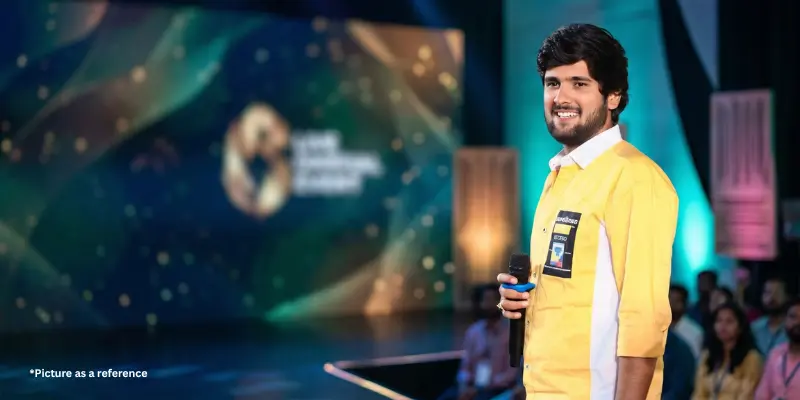 Gujarati singer Gopal Bharwad performing live on stage in a yellow shirt with a modern digital backdrop.
