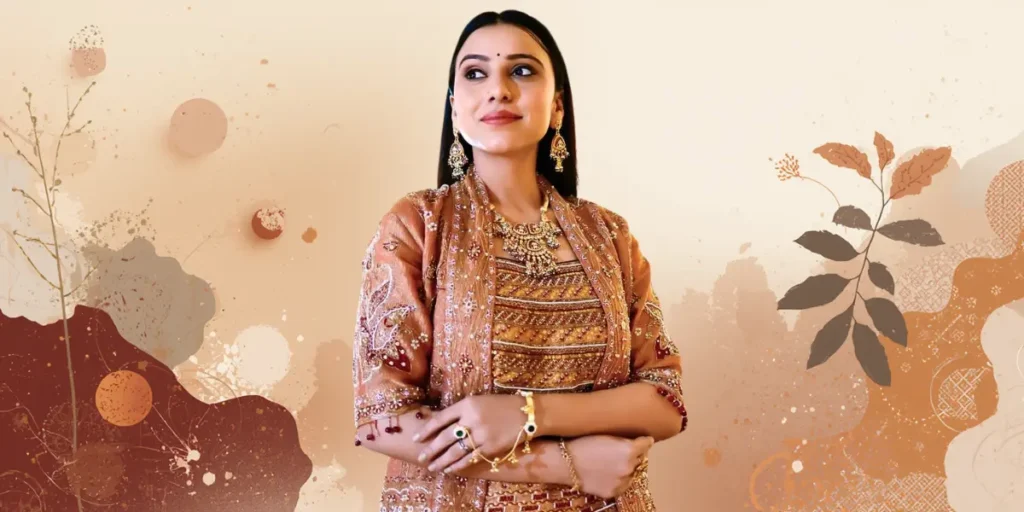 Singer Kinjal Rabari in a richly embellished copper-colored jacket over a brown top, with a heavy kundan necklace and earrings. She is looking to the side with arms crossed.