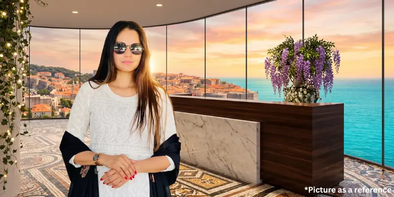 Chini Raval wearing a white chikankari kurta and sunglasses, standing in a luxury coastal balcony overlooking a Mediterranean town at sunset.