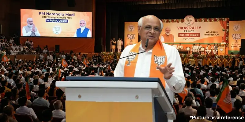 Gujarat CM Bhupendra Patel speaking at the rally, wearing a BJP saffron scarf with a digital backdrop of PM Narendra Modi.
