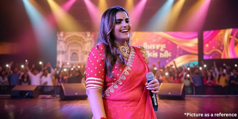 Kajal Maheriya performing live on a concert stage in a pink saree with a microphone.