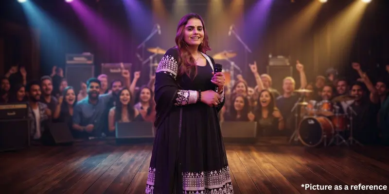 Kajal Maheriya performing in a black Anarkali on a dimly lit, professional concert stage with a crowd in the background.