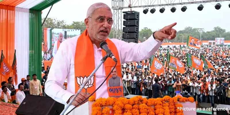 Jagdish Vishwakarma addressing a massive public rally, gesturing towards the crowd from a floral-decorated stage.