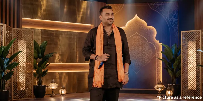 Jignesh Kaviraj performing live on stage in a black kurta and orange dupatta with a decorative backdrop.