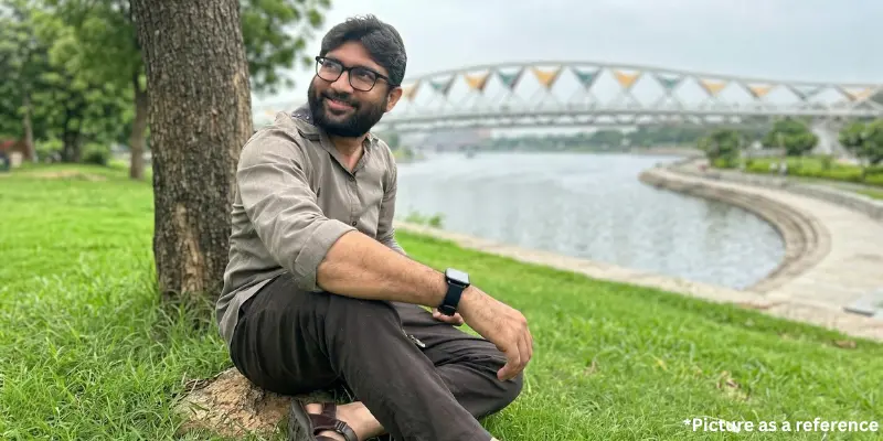 Jignesh Mevani sitting on the grass in a park near the Sabarmati River, with the Atal Bridge visible in the background.