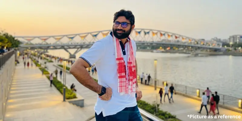 Jignesh Mevani wearing a traditional white and red scarf, standing at the Ahmedabad Riverfront during sunset.