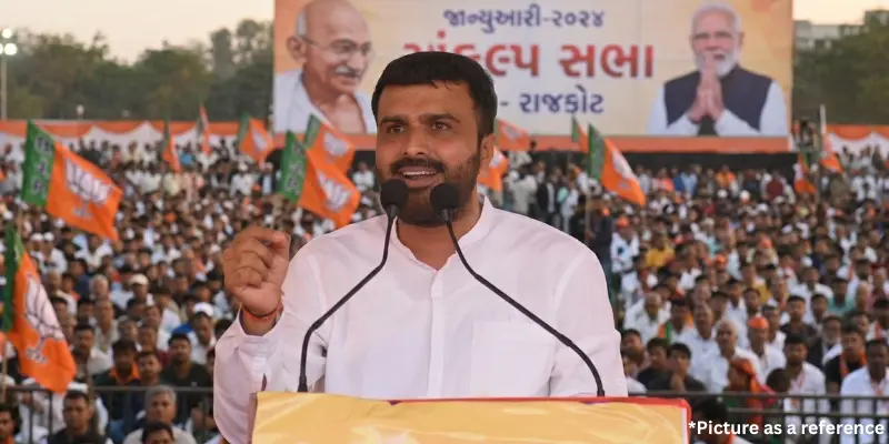 Raju Karpada giving a powerful speech, with a large crowd and party flags in the background.