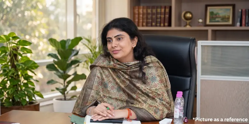 Riva Jadeja in a professional office setting, wearing a patterned shawl while seated at her desk with indoor plants.