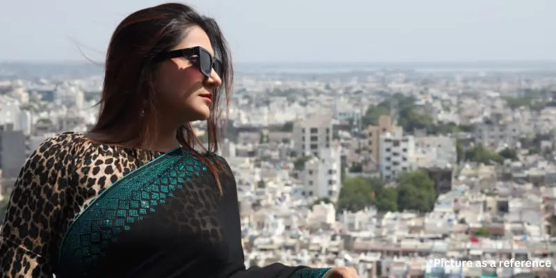 Woman in a black and teal Punjabi-style saree with sunglasses overlooking a city skyline.
