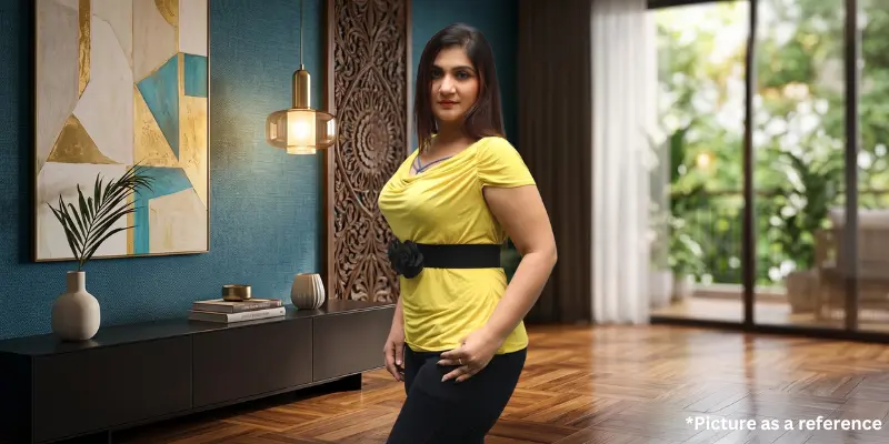 Woman Riya Samani in a yellow top posing in a modern living room with wooden wall decor.