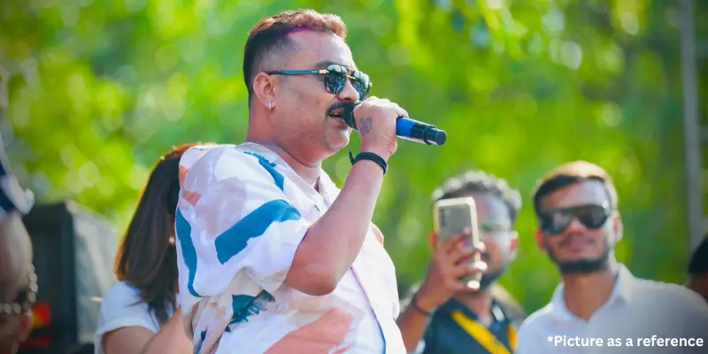 Singer Jignesh Kaviraj singing into a microphone at an outdoor public event, wearing sunglasses and a patterned shirt.