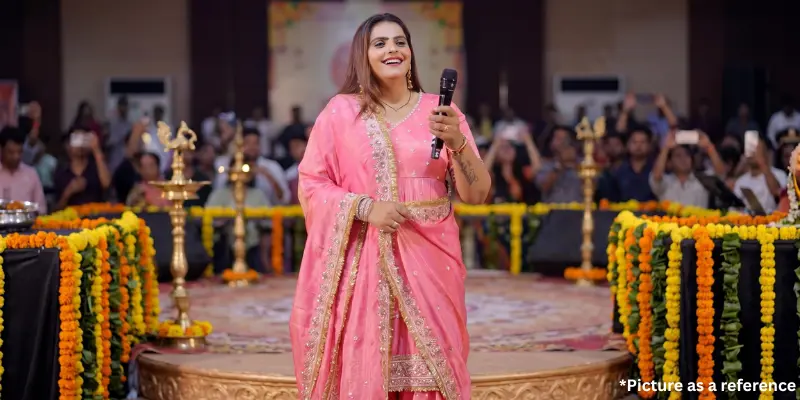 Kajal Maheriya is wearing a pink salwar kameez, with traditional diya lamps and flower garlands in the background.