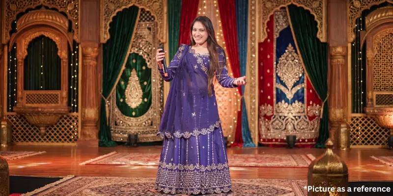 Singer Neha Suthar performing on stage with a microphone, wearing a purple embroidered lehenga choli.
