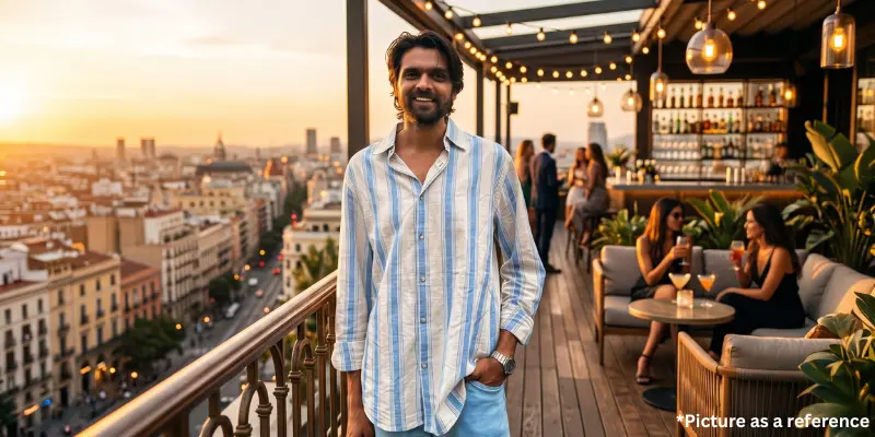 Karan Joshi smiling in a light blue and white striped shirt on a luxurious rooftop bar overlooking a city skyline at sunset.