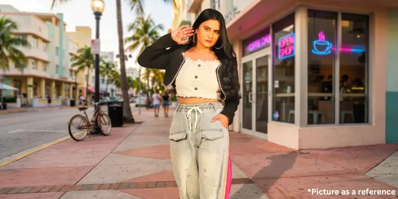 Singer Zeel Joshi dressed in a white crop top, black jacket, and light-wash cargo jeans, posing on a city sidewalk.